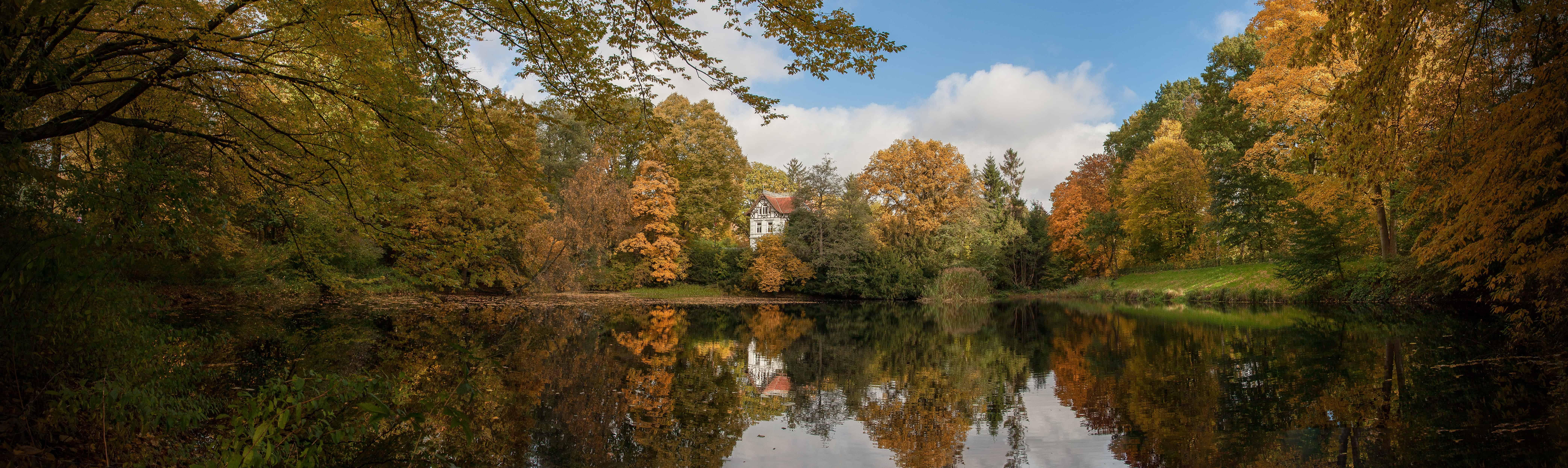 Der Herbst im Park mit Blick auf den ruhigen Fluss und bunte Laubbäume.