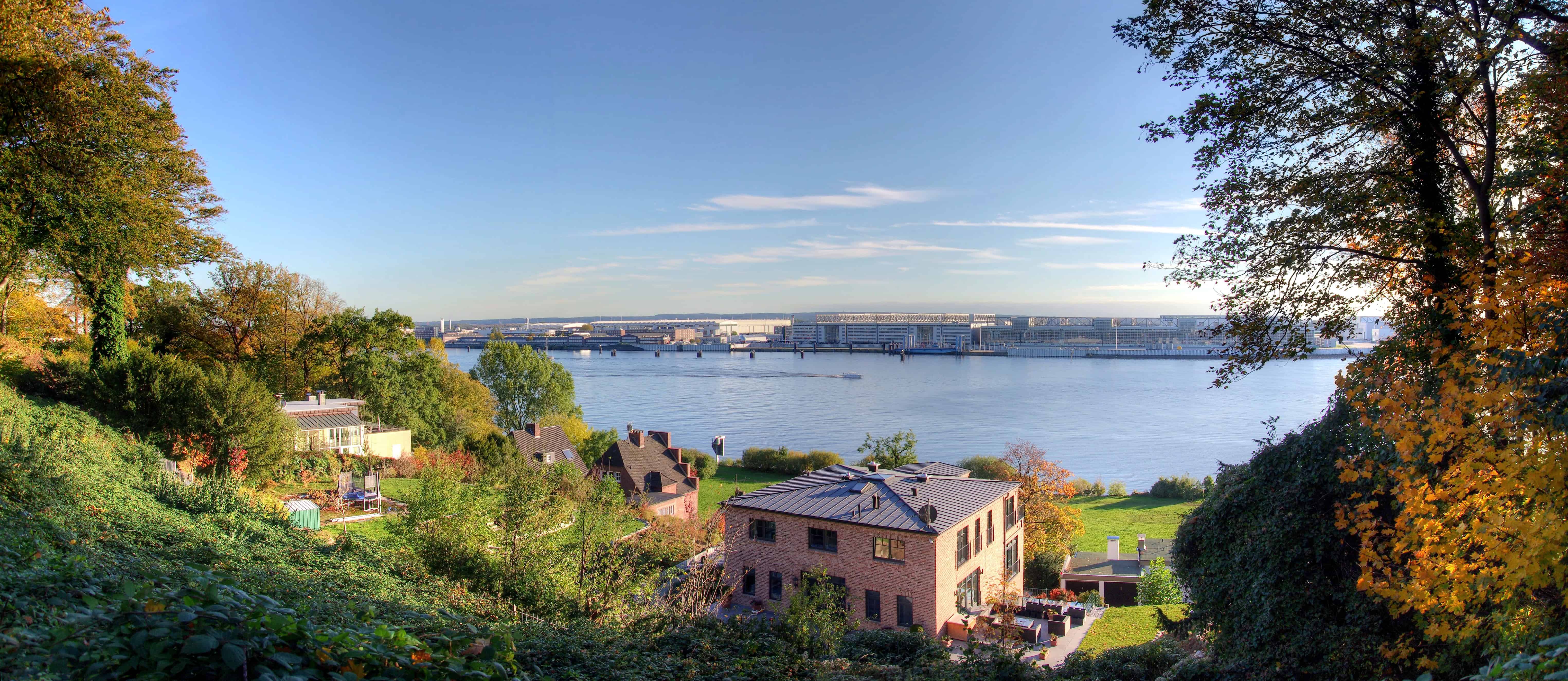 Hafenblick auf Hamburg mit modernen Häusern und grüner Natur, sonniger Himmel, ruhige Wohnlage.