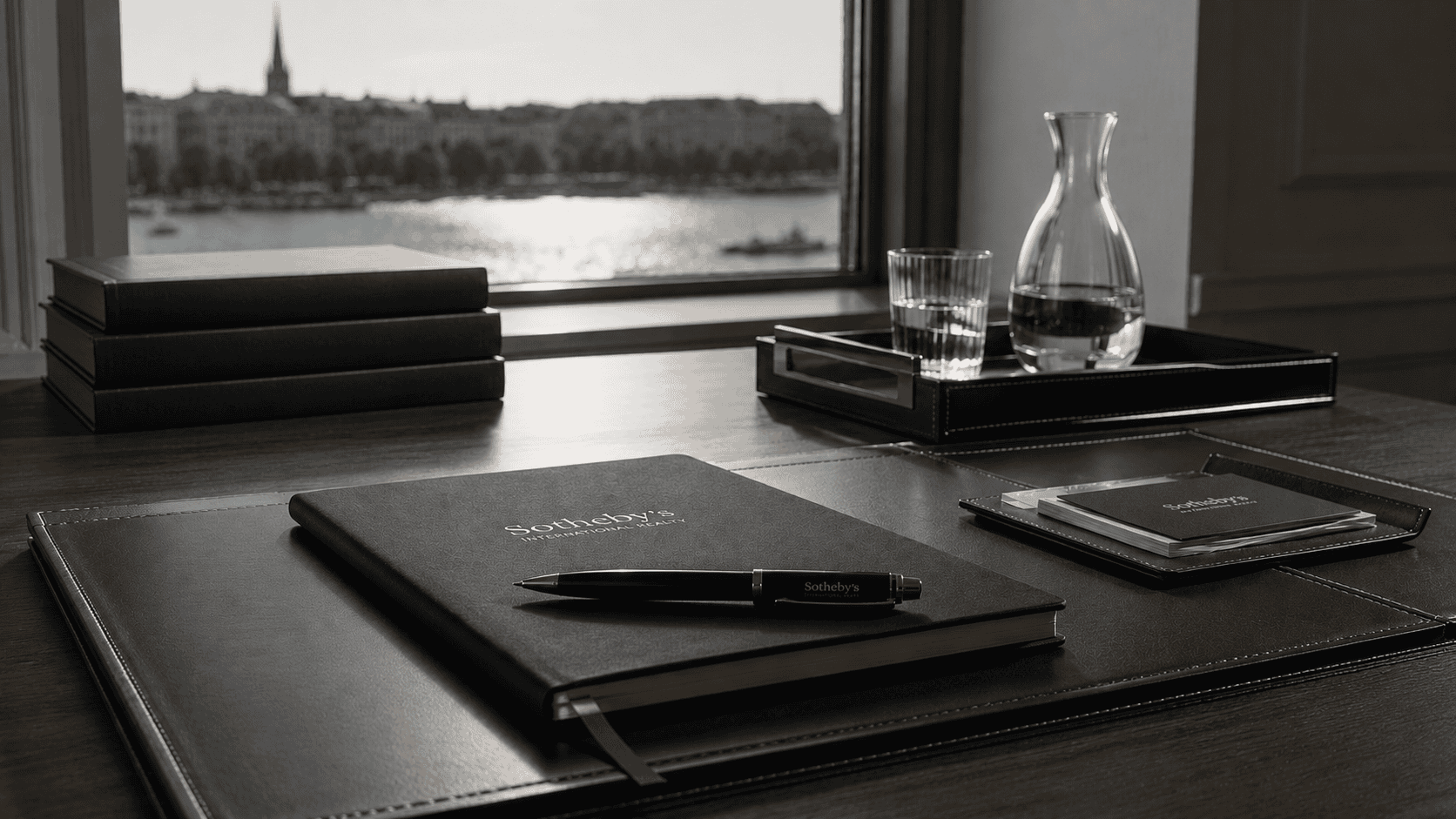 Eleganter Schreibtisch mit Notizbuch, Stift und Wasserkrug vor Fenster mit Blick auf Hamburg.