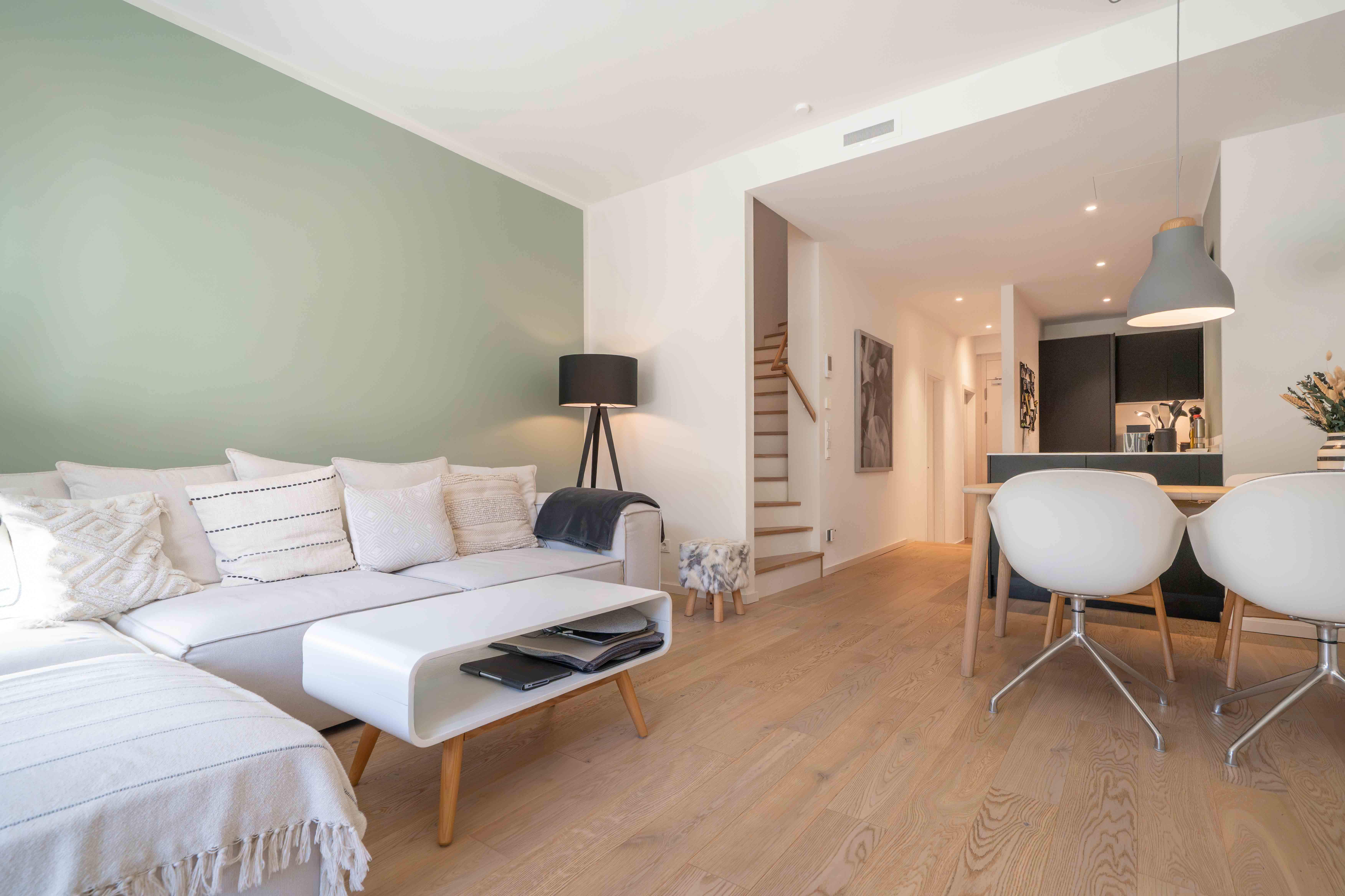 Helles Wohnzimmer mit grüner Wand, Sofa und Essbereich in Hamburg.