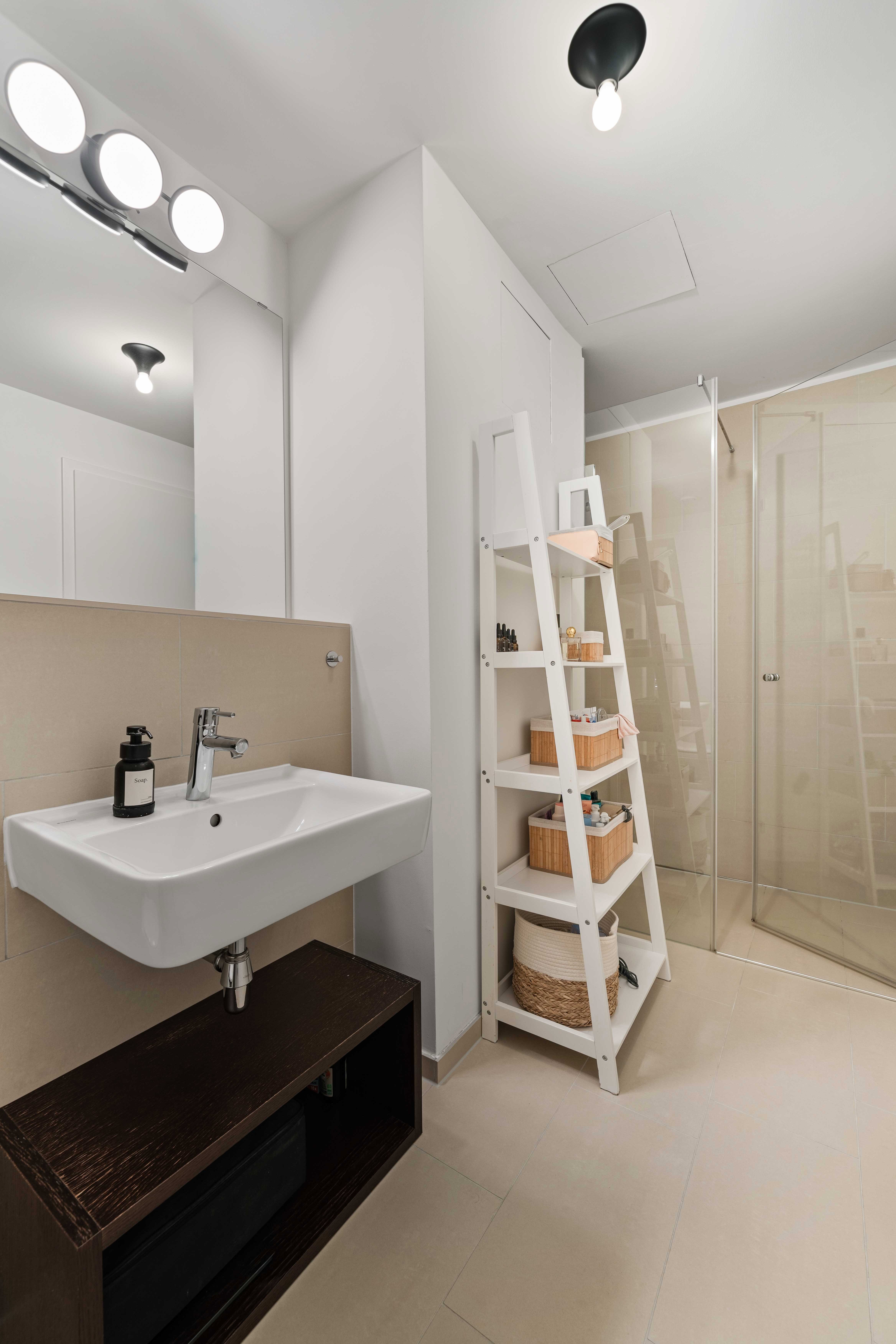 Helles Badezimmer mit Waschbecken, Spiegel und Regalen.